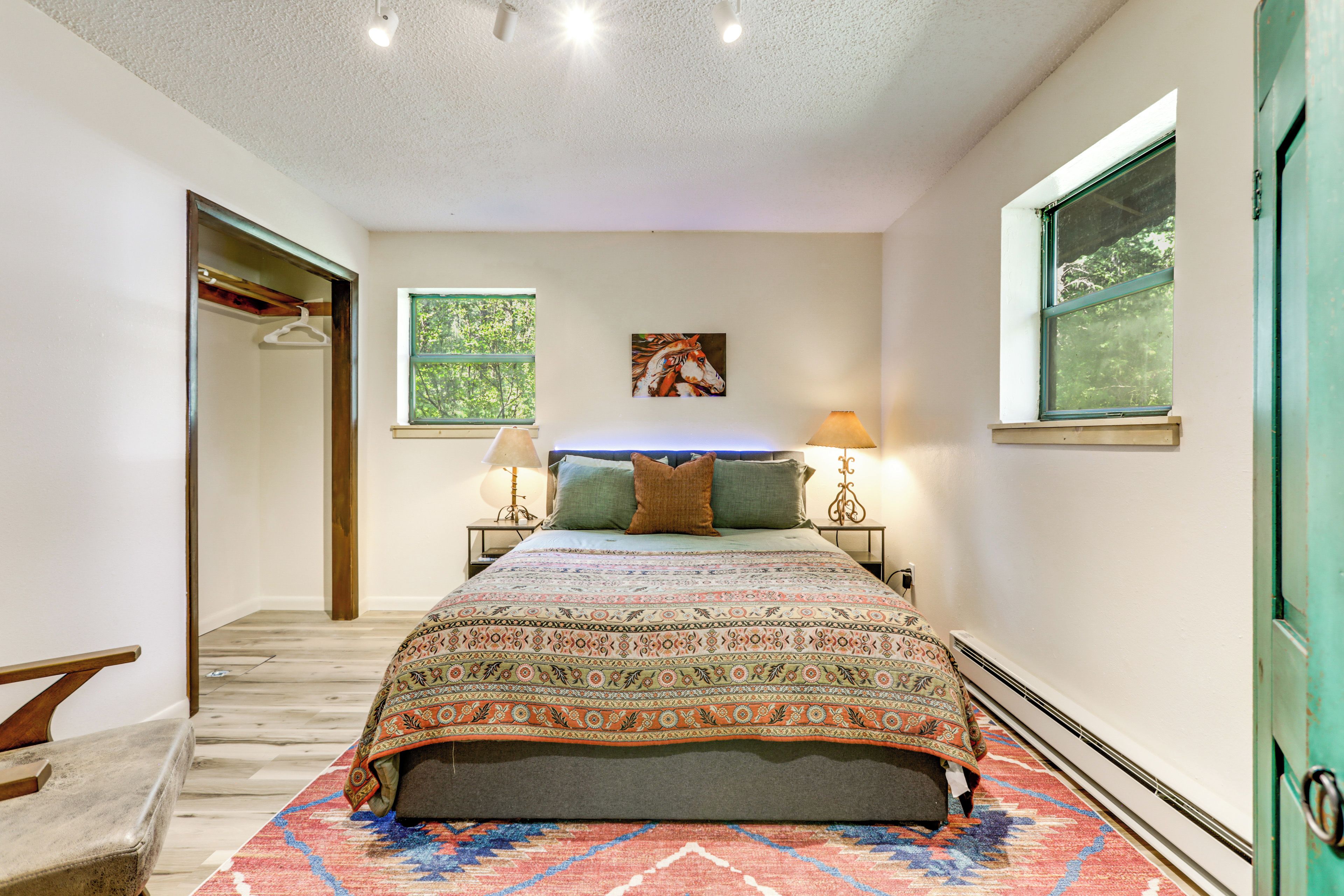 A bedroom with a bed, two bedside tables, a hanging lamp, a painting, and a window.