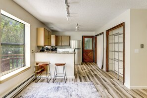 Une cuisine avec des meubles en bois, un plan de travail blanc et un réfrigérateur encastré. On y trouve deux tabourets de bar et une grande fenêtre qui offre une vue sur l’extérieur.