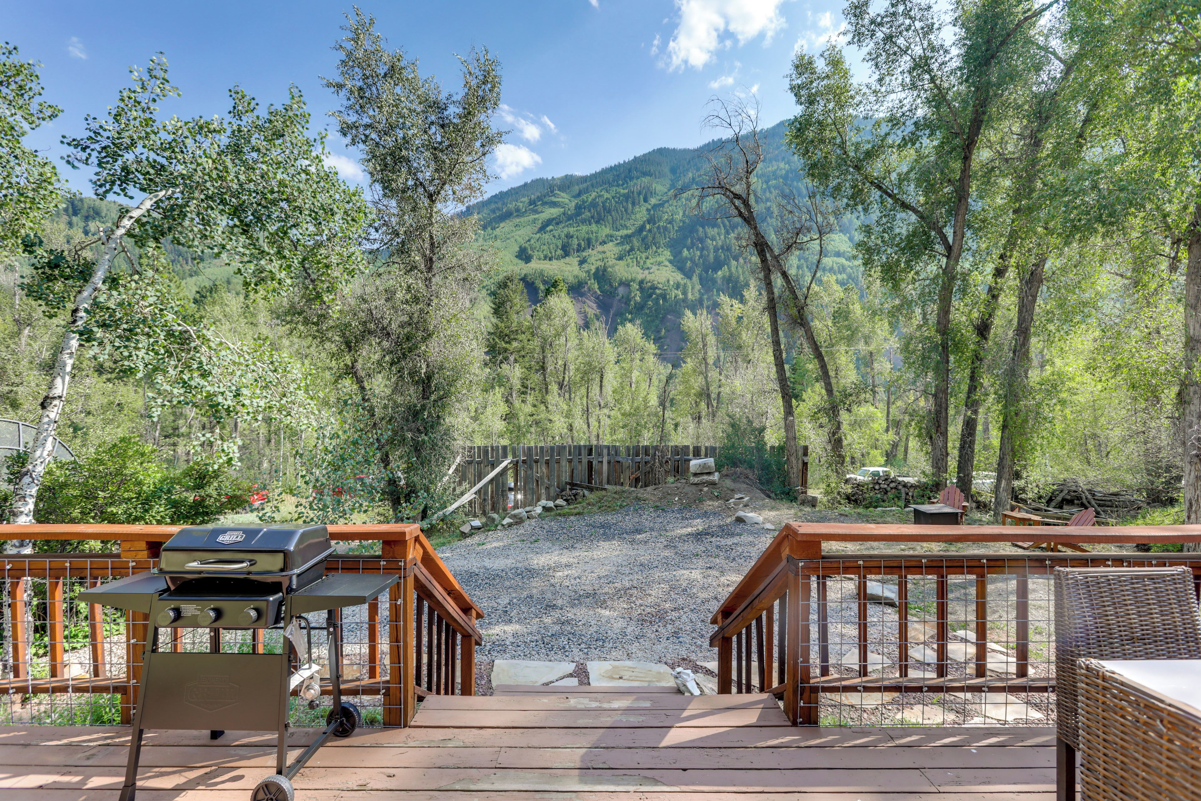A wooden deck leading to a forested area with a view of a mountain range.