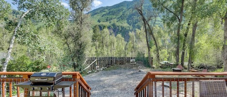 A wooden deck leading to a forested area with a view of a mountain range.
