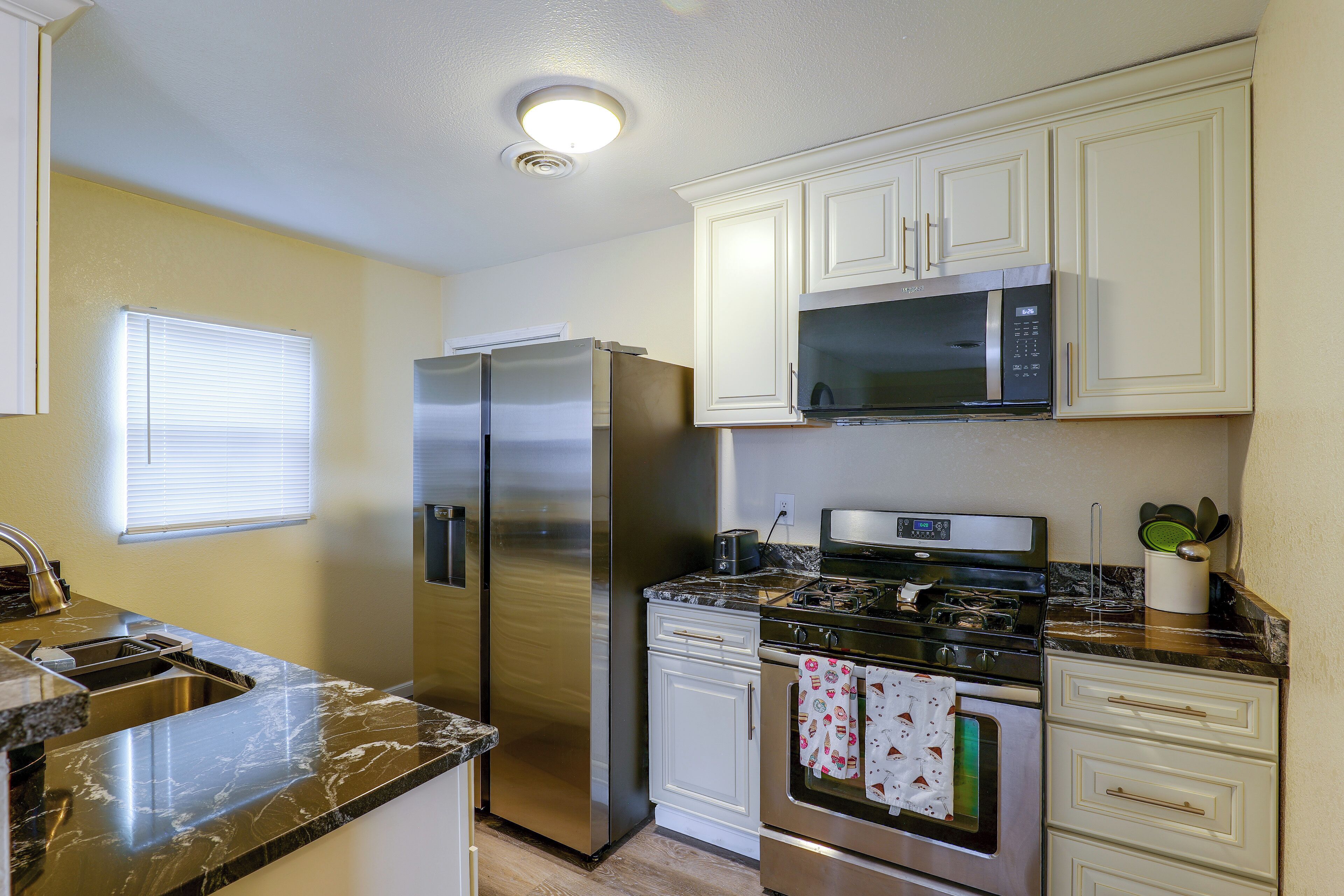 Una cocina con refrigerador de acero inoxidable, microondas, horno y lavamanos.