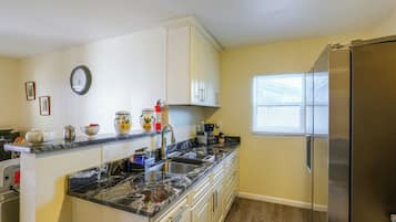 A kitchen with a marble countertop, stainless steel appliances, and a window with blinds.