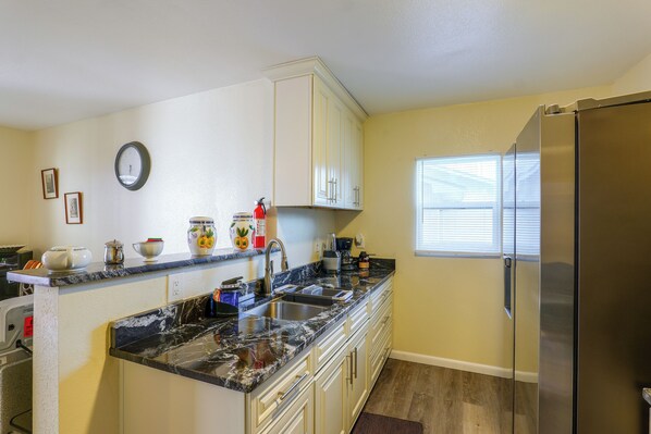 A kitchen with a marble countertop, stainless steel appliances, and a window with blinds.