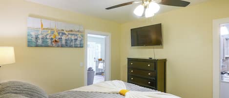A bedroom with a bed, a ceiling fan, a painting, a dresser, and a television.
