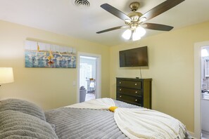 A bedroom with a bed, a ceiling fan, a painting, a dresser, and a television.