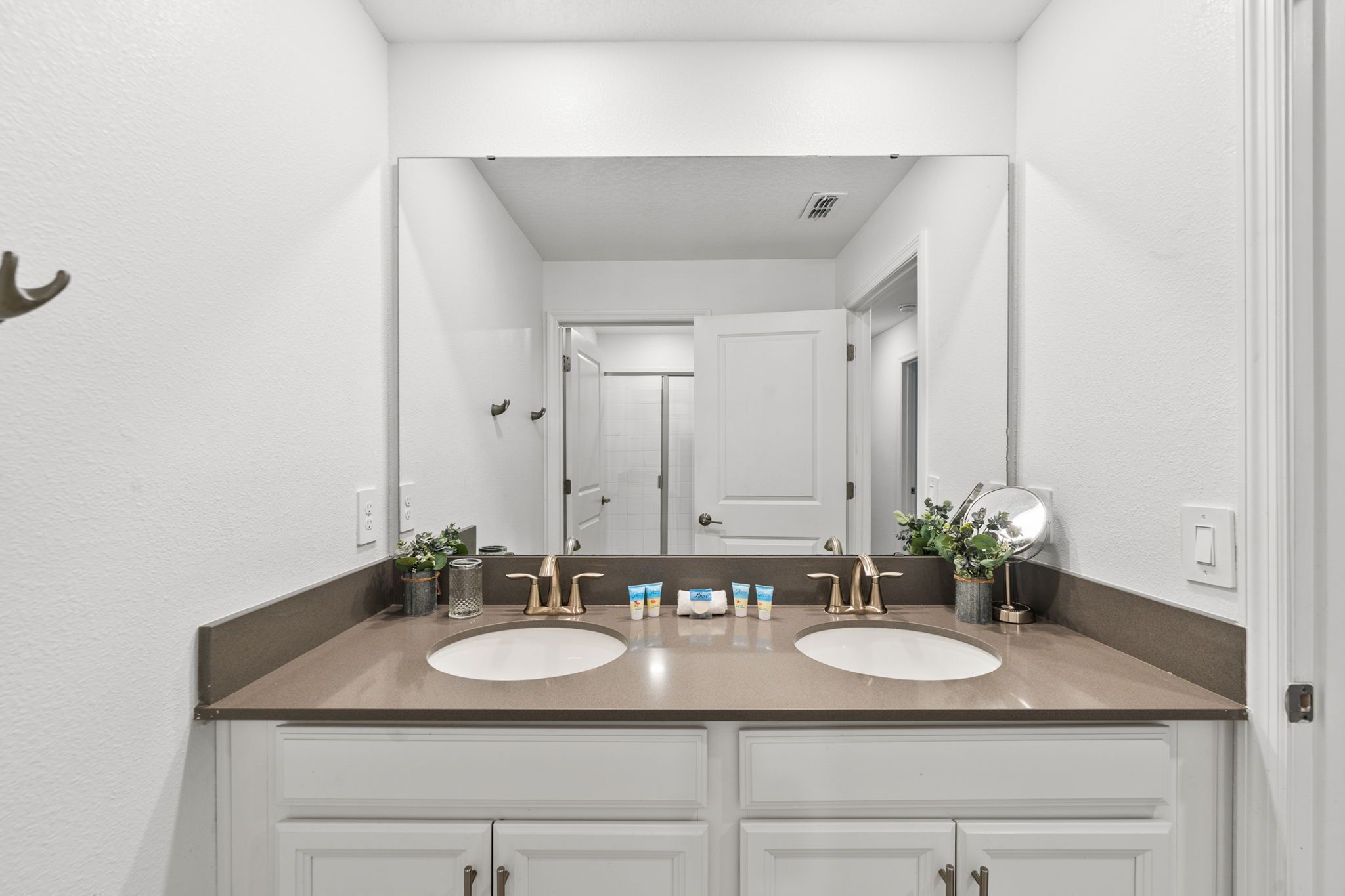 A bathroom with two sinks, a large mirror, and a shower visible through an open door.
