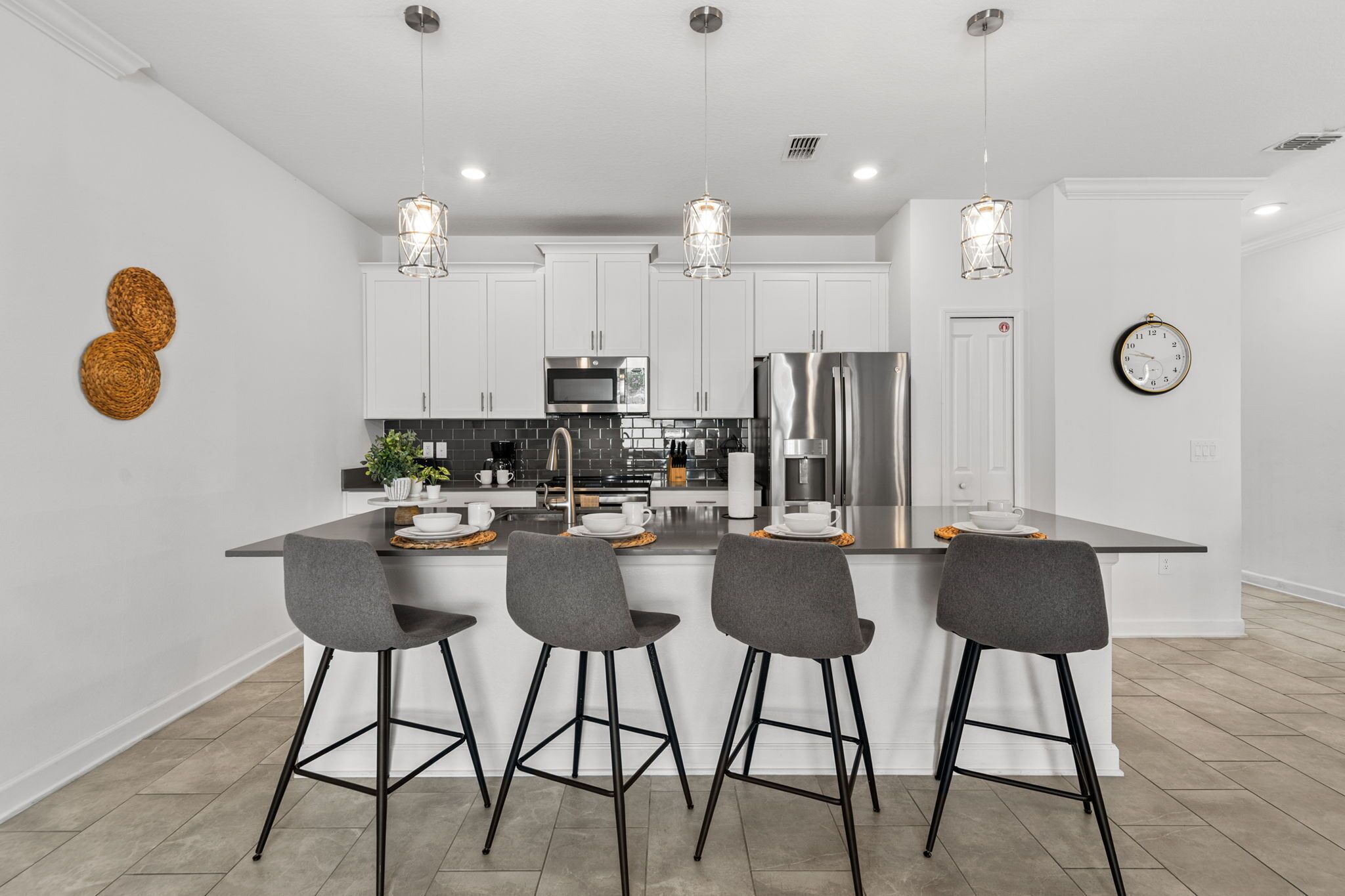 A modern kitchen with a central island, bar stools, stainless steel appliances, pendant lighting, and a clock on the wall.