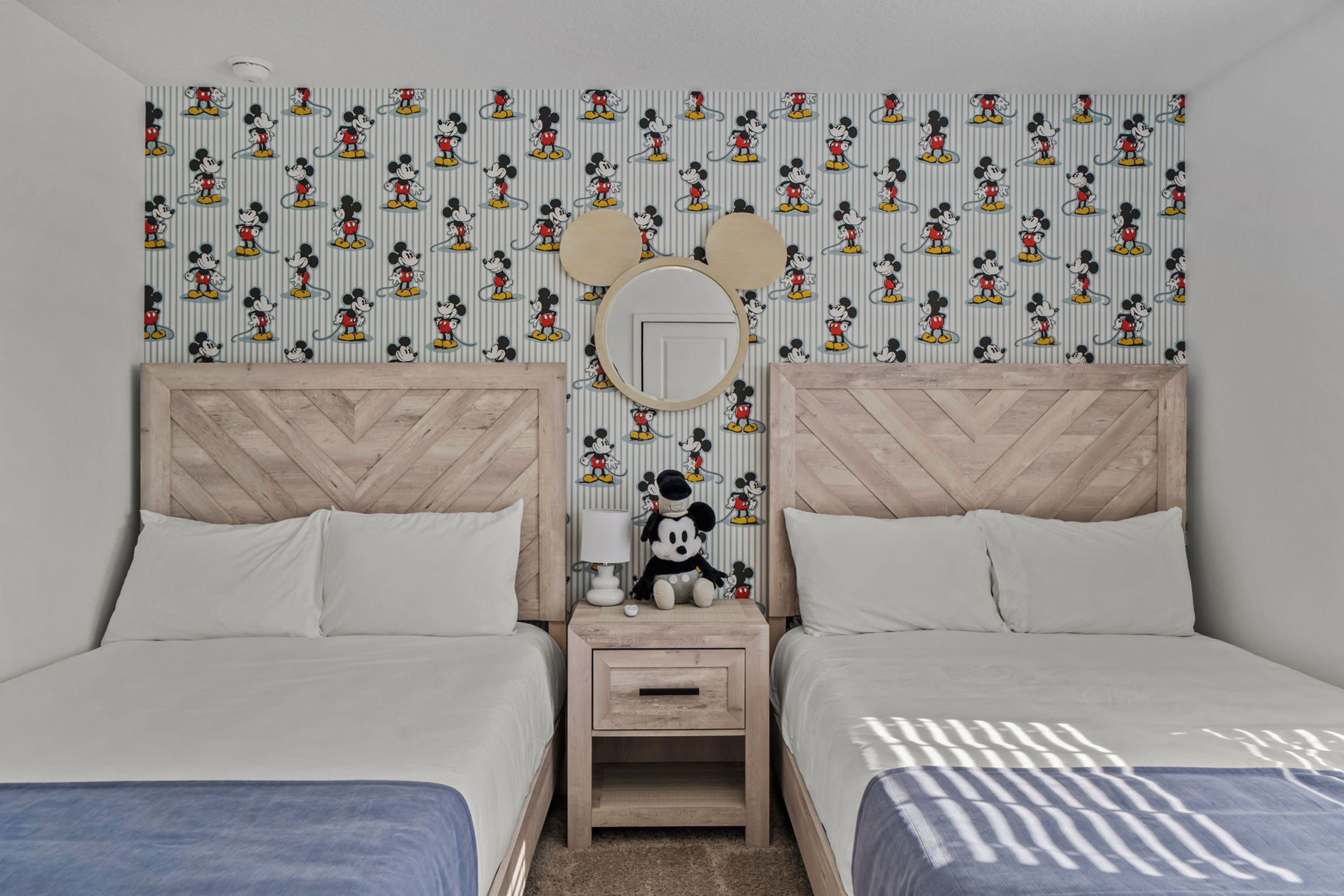 Et soveværelse med to senge, et natbord med et spejl og Mickey Mouse tapet.