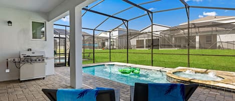 An outdoor patio with a pool, two chairs, a grill, and a hot tub.