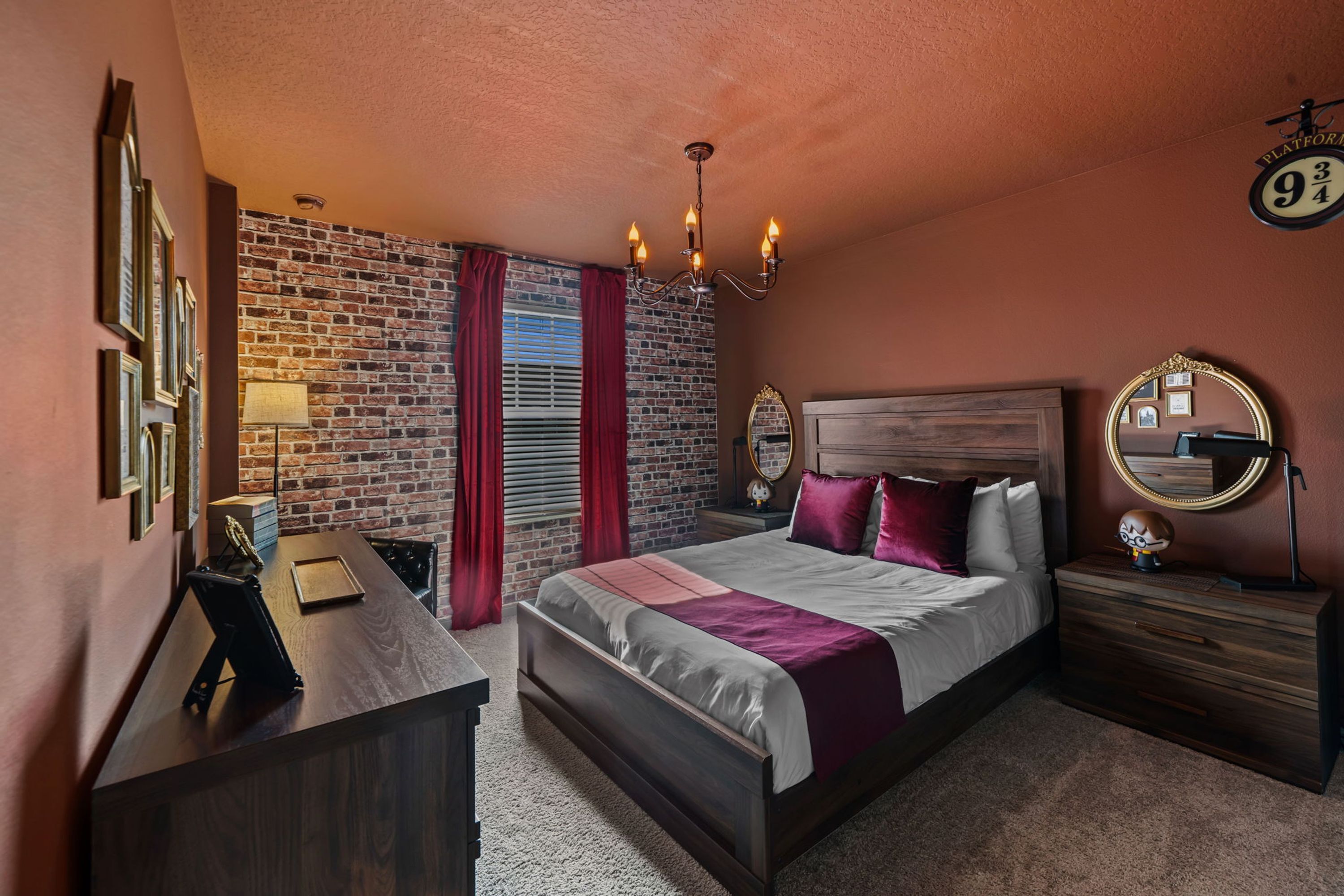 Un dormitorio con pared de ladrillo, una cama con cabecera de madera, un escritorio con lámpara y una mesita de noche con espejo.