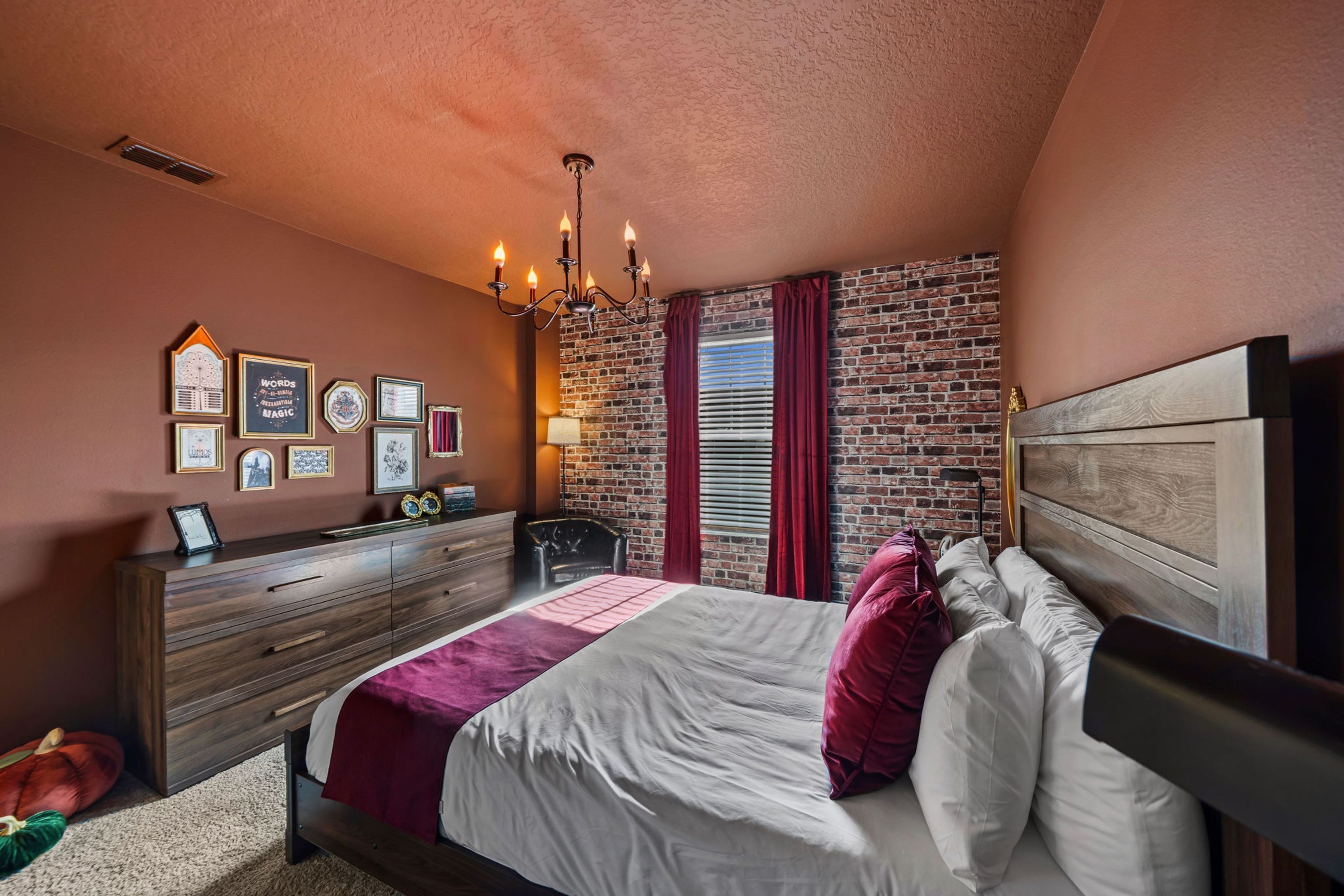 Un dormitorio con pared de ladrillo, cómoda de madera, cama con ropa de cama blanca y roja, y un candelabro.