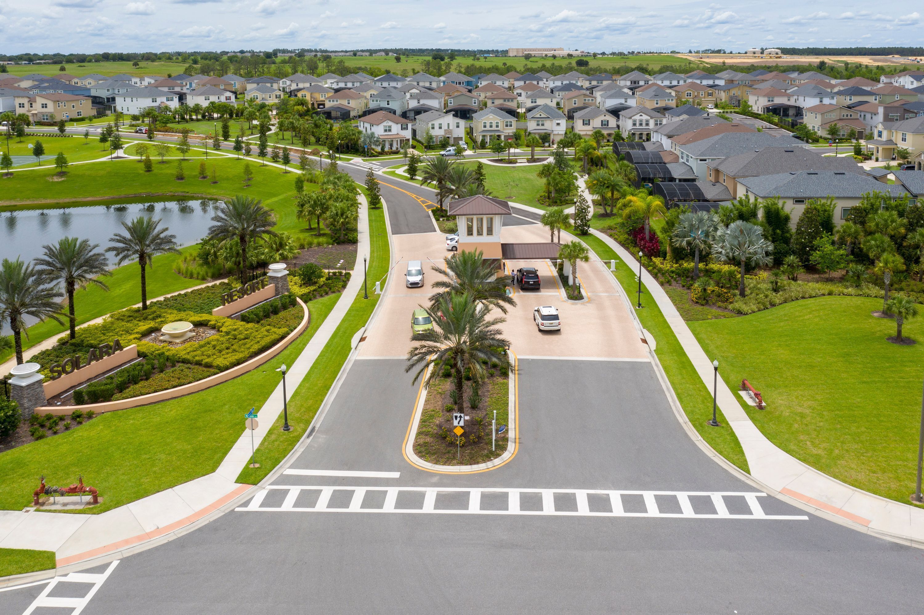 A residential area with a curved road, a body of water, and houses with a central building that appears to be a community center or clubhouse.
