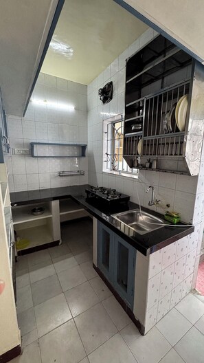 A compact kitchen with a gas stove, sink, and a window with a view. - Fully Furnished 2BHK in Anna Nagar Near Hospitals and IVF Centres (Chennai)