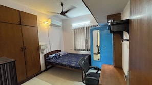 A compact room with a bed, a desk, a chair, a wardrobe, and a ceiling fan. - Fully Furnished 2BHK in Anna Nagar Near Hospitals and IVF Centres (Chennai)