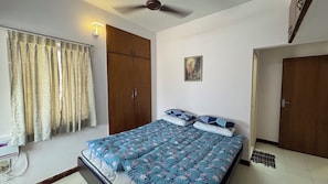 A bedroom with a bed, curtains, a ceiling fan, a door, and a wall-mounted light.