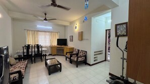 A living room with a dining area, a TV, ceiling fans, and a staircase leading to another level.