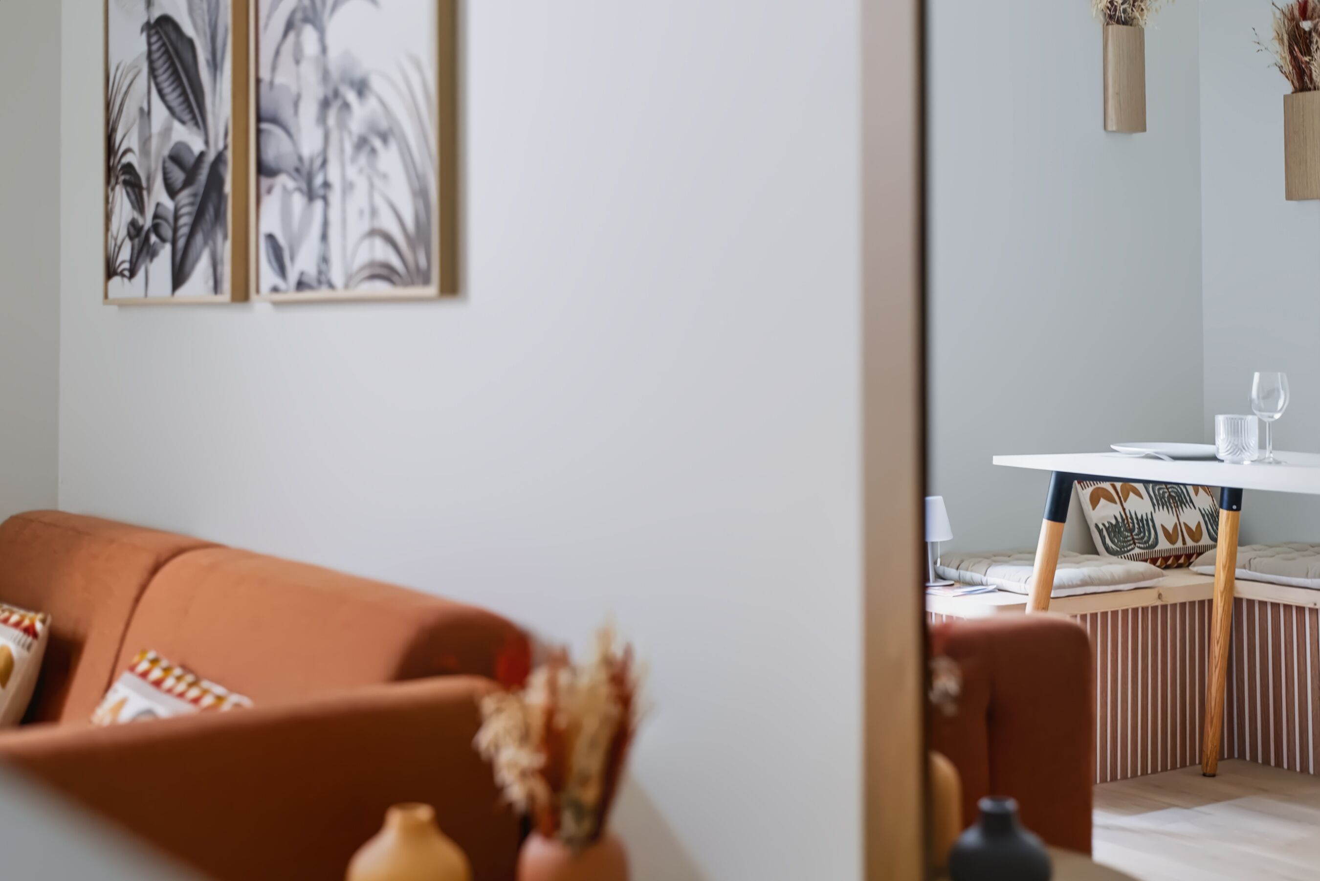 En moderne stue med en sofa, et spisebord med stole og en vase med tørrede blomster.