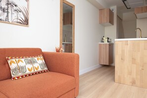 A modern living room with a sofa, a decorative pillow, and a kitchen area with wooden cabinets and a countertop. - Apartment with a private courtyard • Cathedral, 15 minutes away • Air Conditioning • Free parking (Albi)