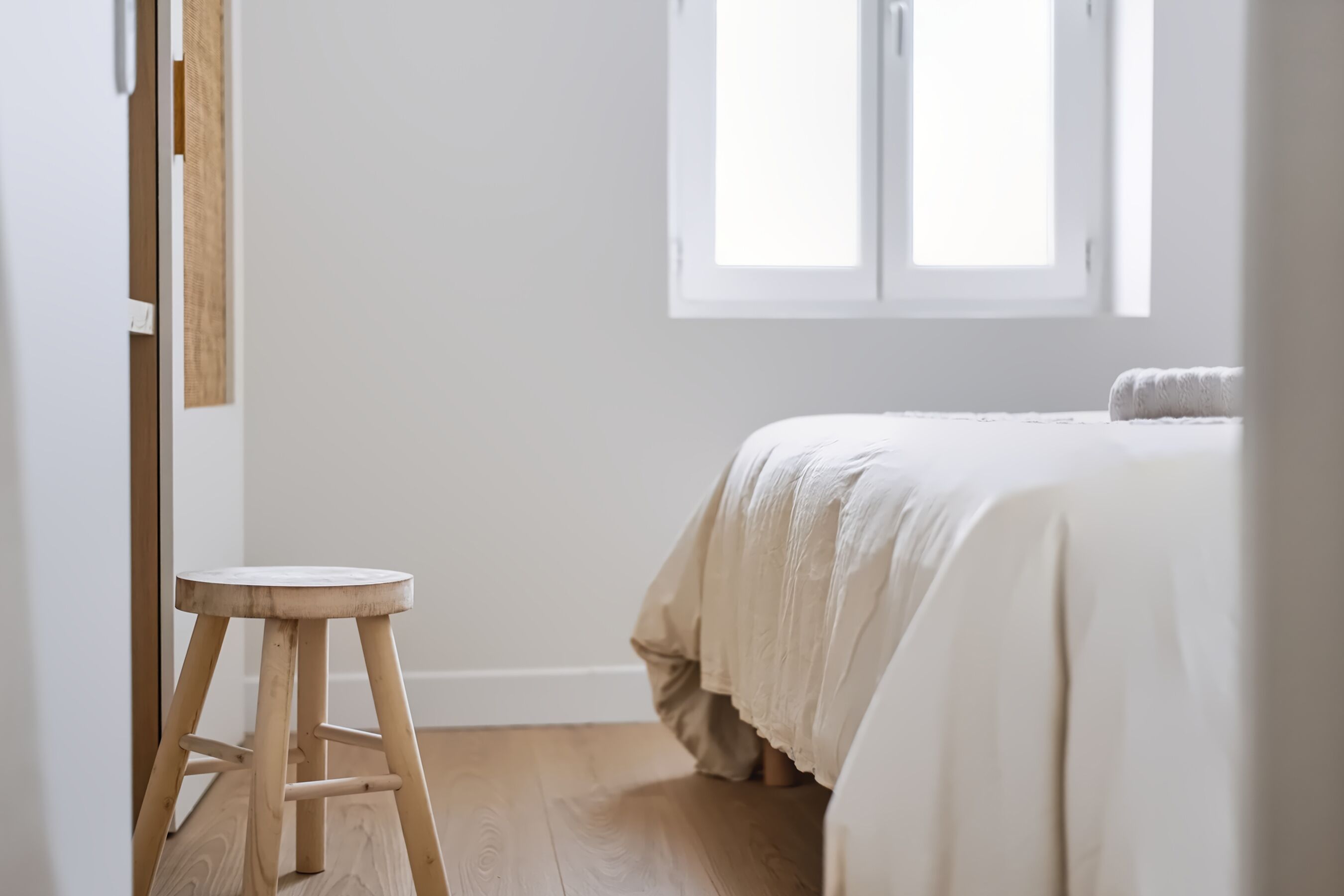 Una camera da letto con un letto, uno sgabello di legno e una finestra.