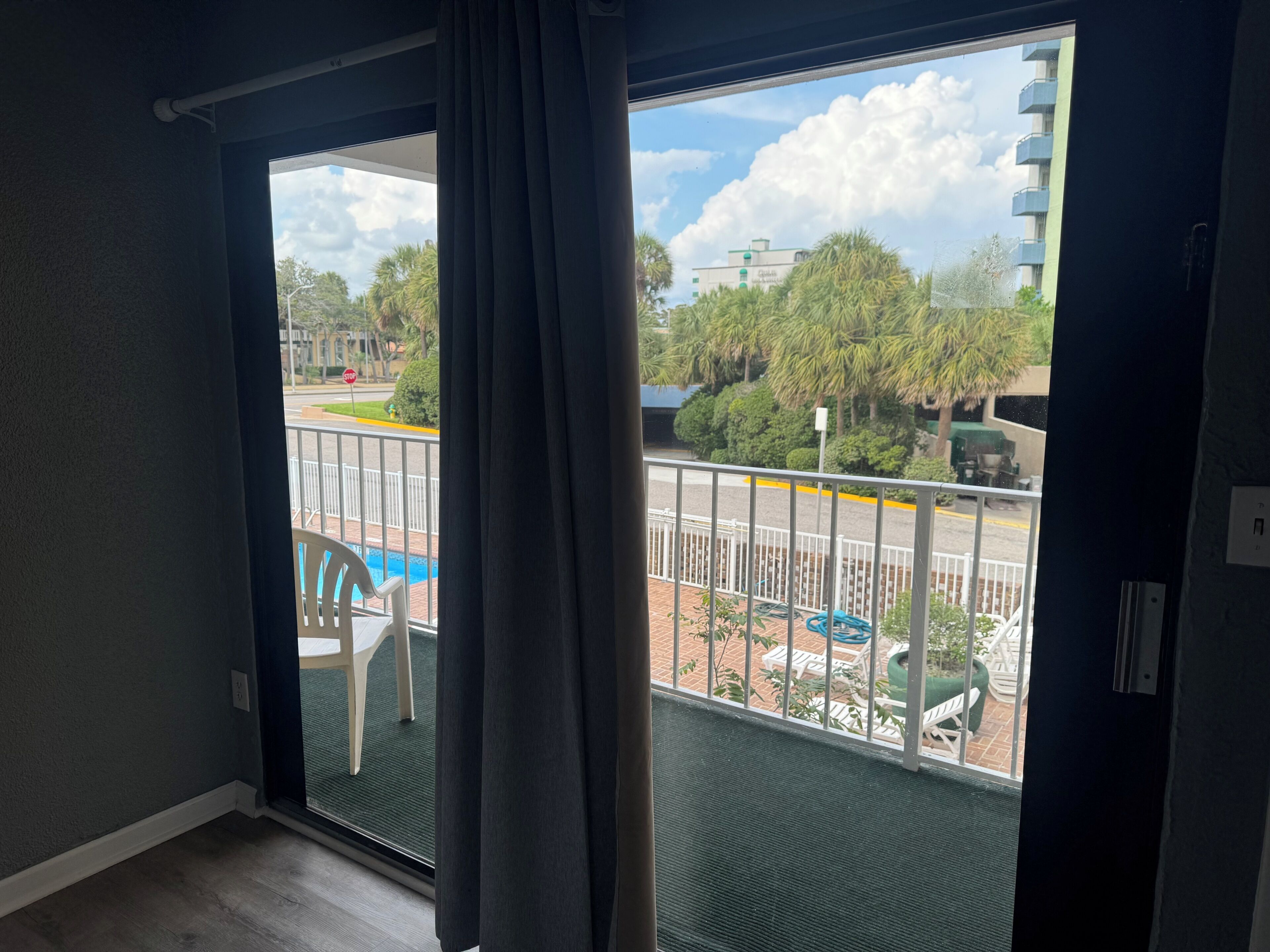 Quarto com porta de vidro deslizante que dá para uma varanda com vista para a rua, árvores e um edifício.