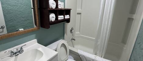 Une salle de bain avec un lavabo, des toilettes et une douche. On y trouve un porte-serviettes avec des serviettes et un miroir au-dessus du lavabo.
