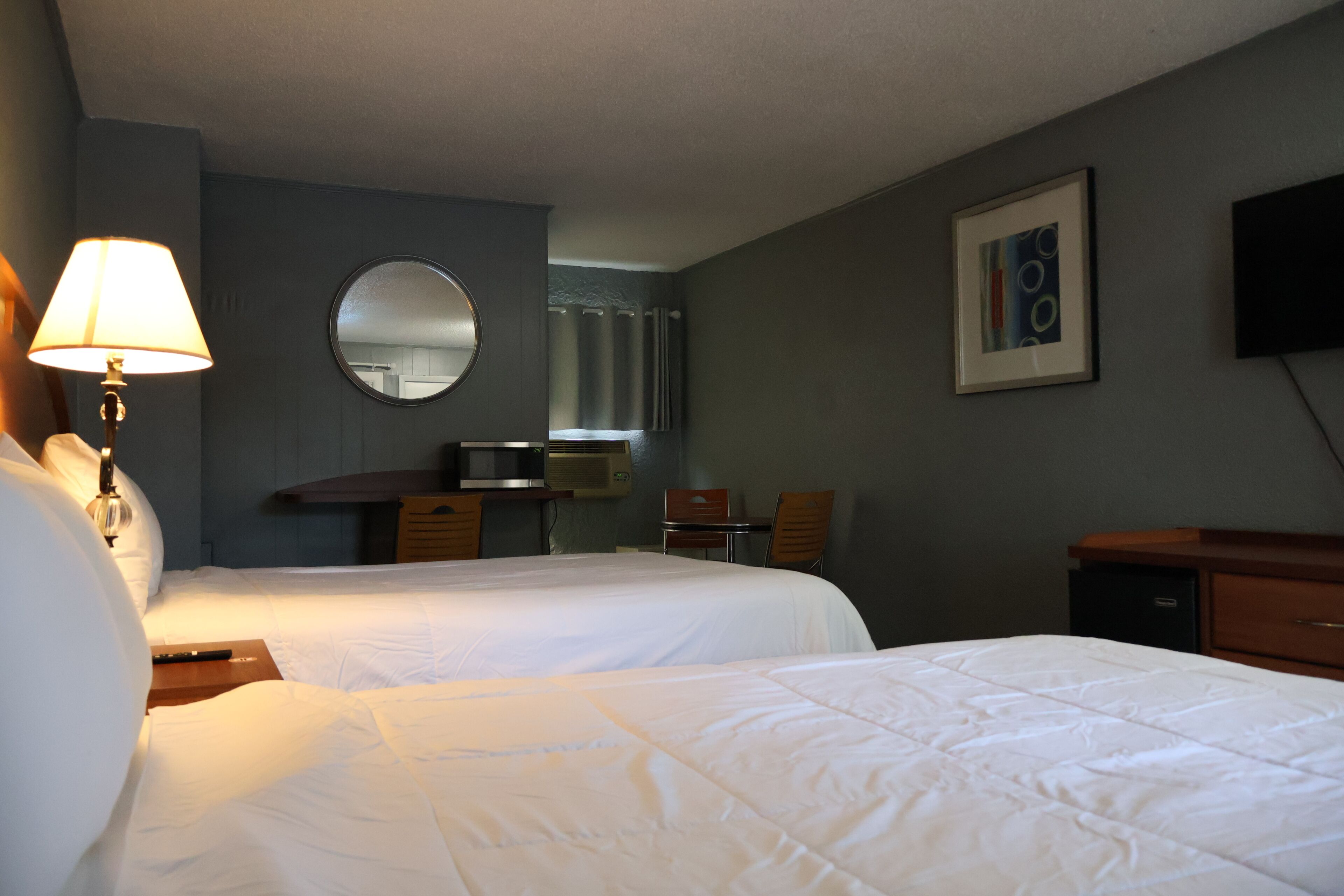 A hotel room with two beds, a desk, a chair, a television, and a mirror.