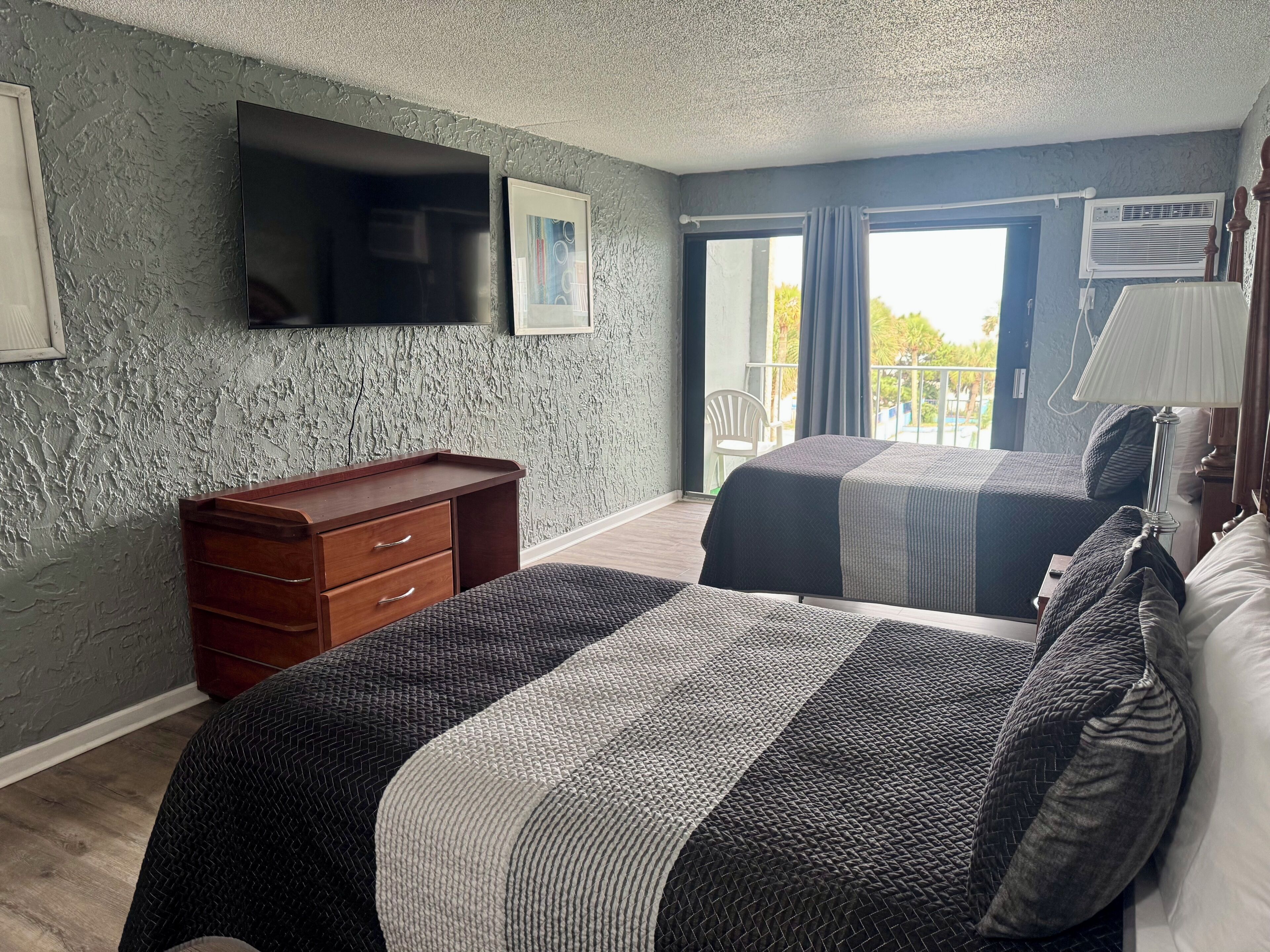 Ein Hotelzimmer mit Bett, Schminktisch, Fernseher und Balkon mit Stuhl.
