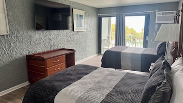 Una habitación de hotel con cama, cómoda, televisor y balcón con una silla.