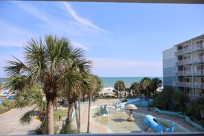 A view of a beach resort with palm trees, a pool area with a dinosaur statue, and a building with balconies. - Ocean 12 Beach Hotel (Myrtle Beach)