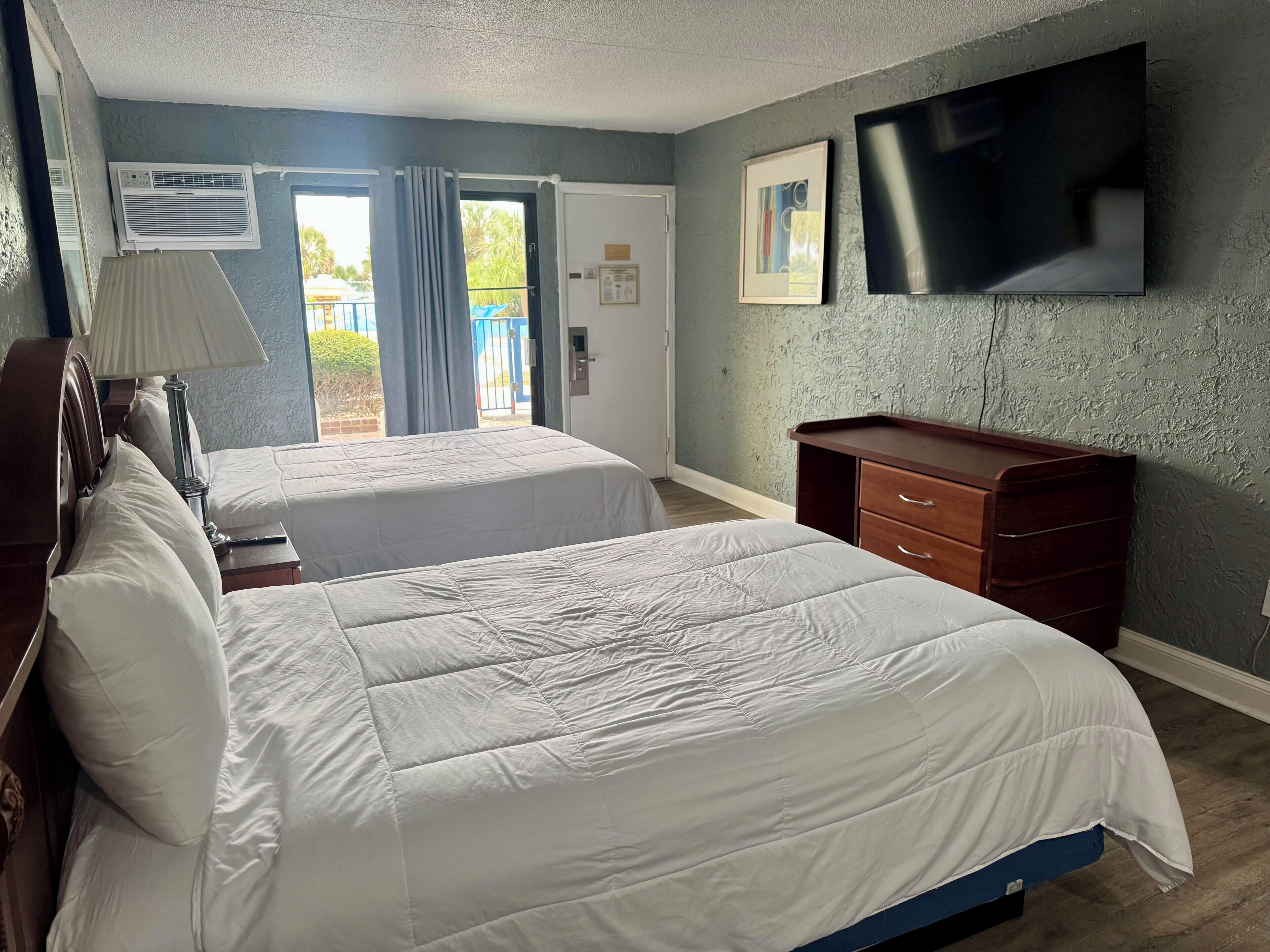 Habitación de hotel con dos camas, un tocador, un televisor de pantalla plana y un aire acondicionado.