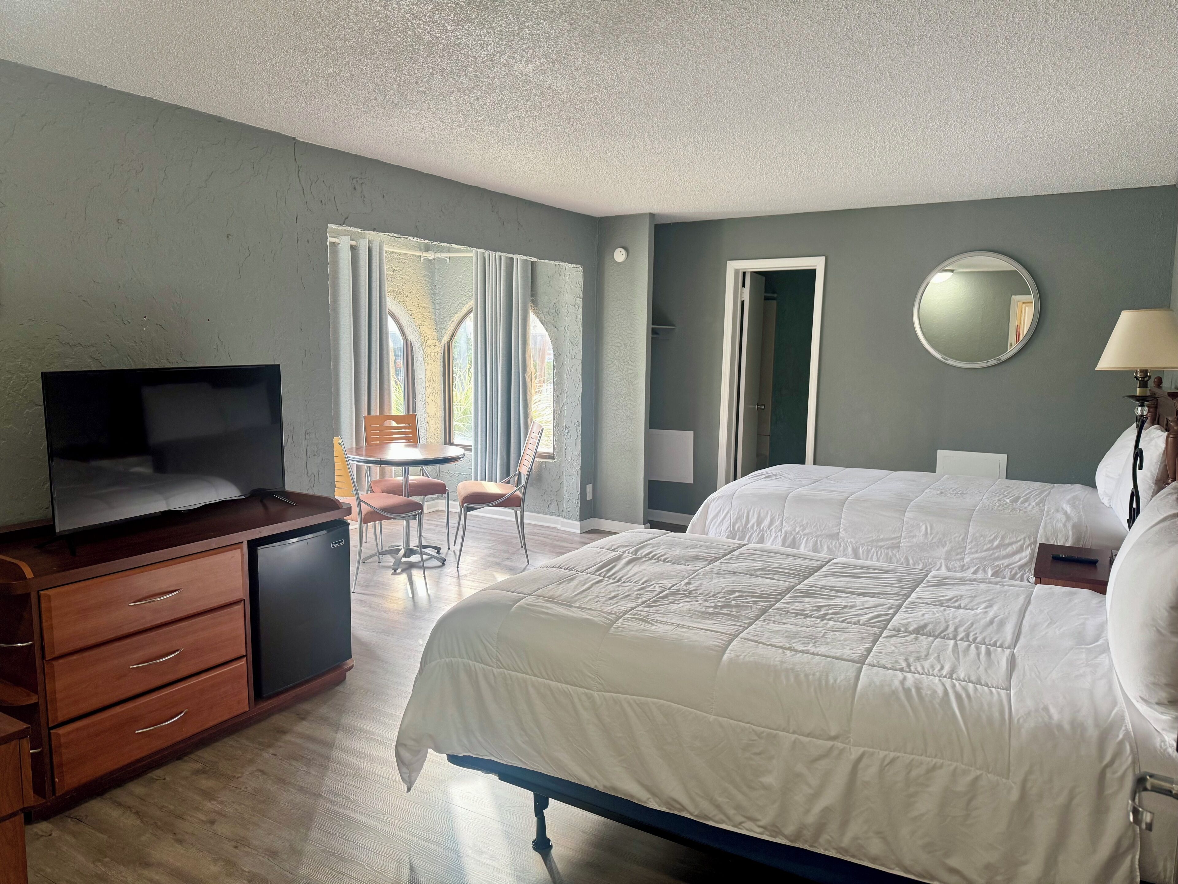 A hotel room with a bed, a desk with a television, a chair, and a window with curtains.