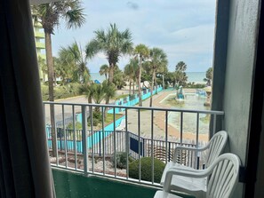 Un balcón con vistas a una playa, palmeras y una piscina con una estatua.