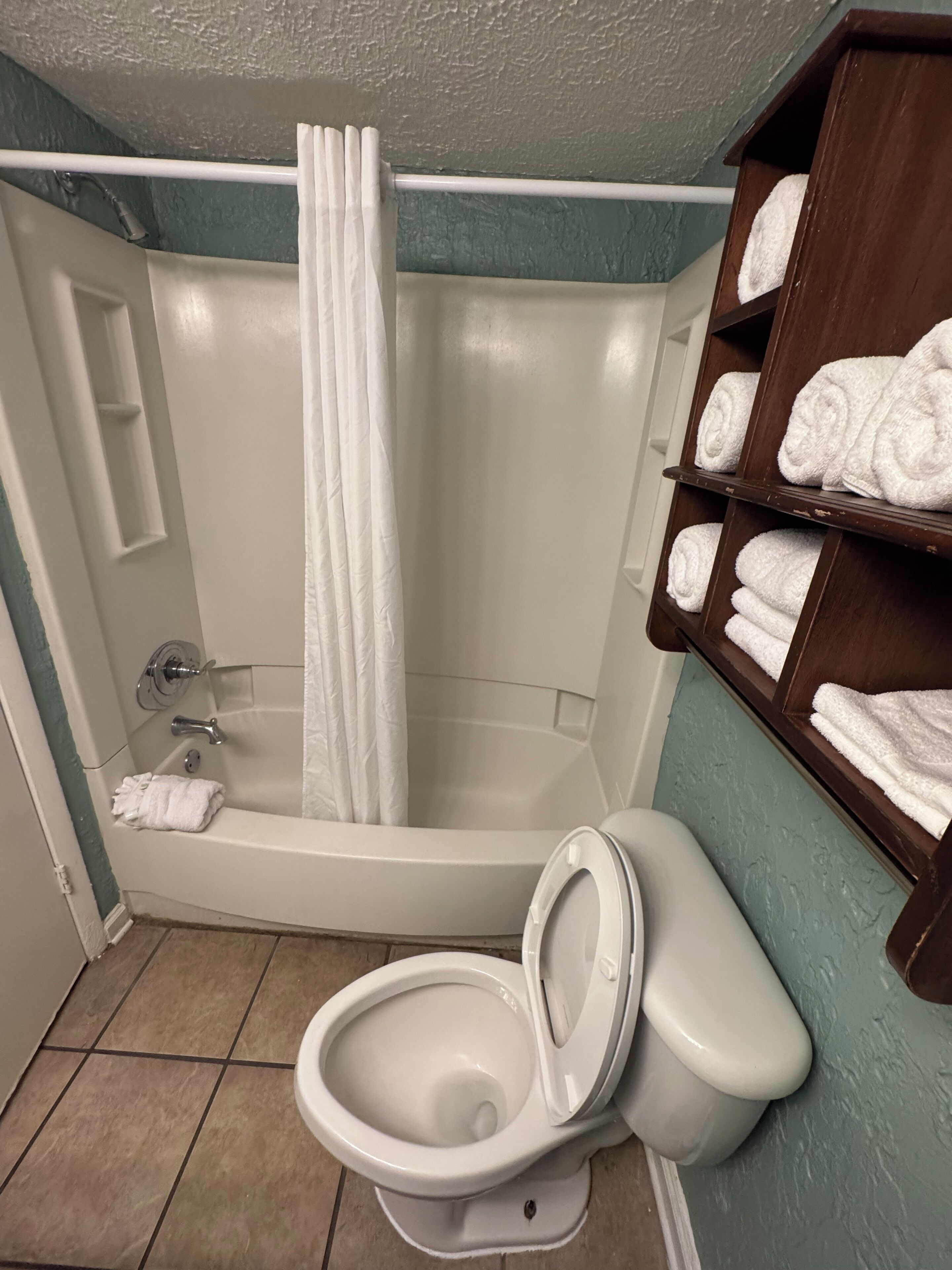 Ein Badezimmer mit Badewanne, Toilette und Regalen mit Handtüchern.