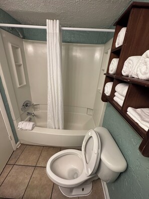 Un baño con bañera, inodoro y repisas con toallas.