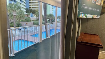 Uma varanda com piscina, vista de um edifício de hotel e uma televisão exibindo um programa.
