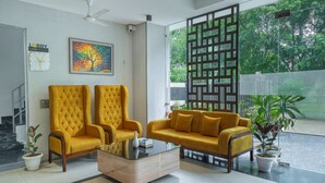 Un vestíbulo moderno con dos sillones amarillos, una mesa de centro, un cuadro, un reloj y vistas al exterior con vegetación.