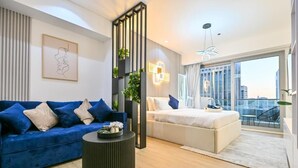 Una sala de estar moderna con un sofá azul, una mesa de centro redonda y una cama con cabecera blanca.