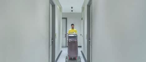 A person in a yellow shirt pushing a cart with water bottles down a hallway with doors on either side.