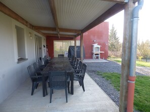 An outdoor patio with a long table and chairs, a barbecue grill, and a covered area with a chimney.