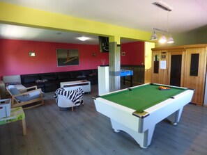 Una habitación con mesa de billar, sofá, sillón y aparador de madera.