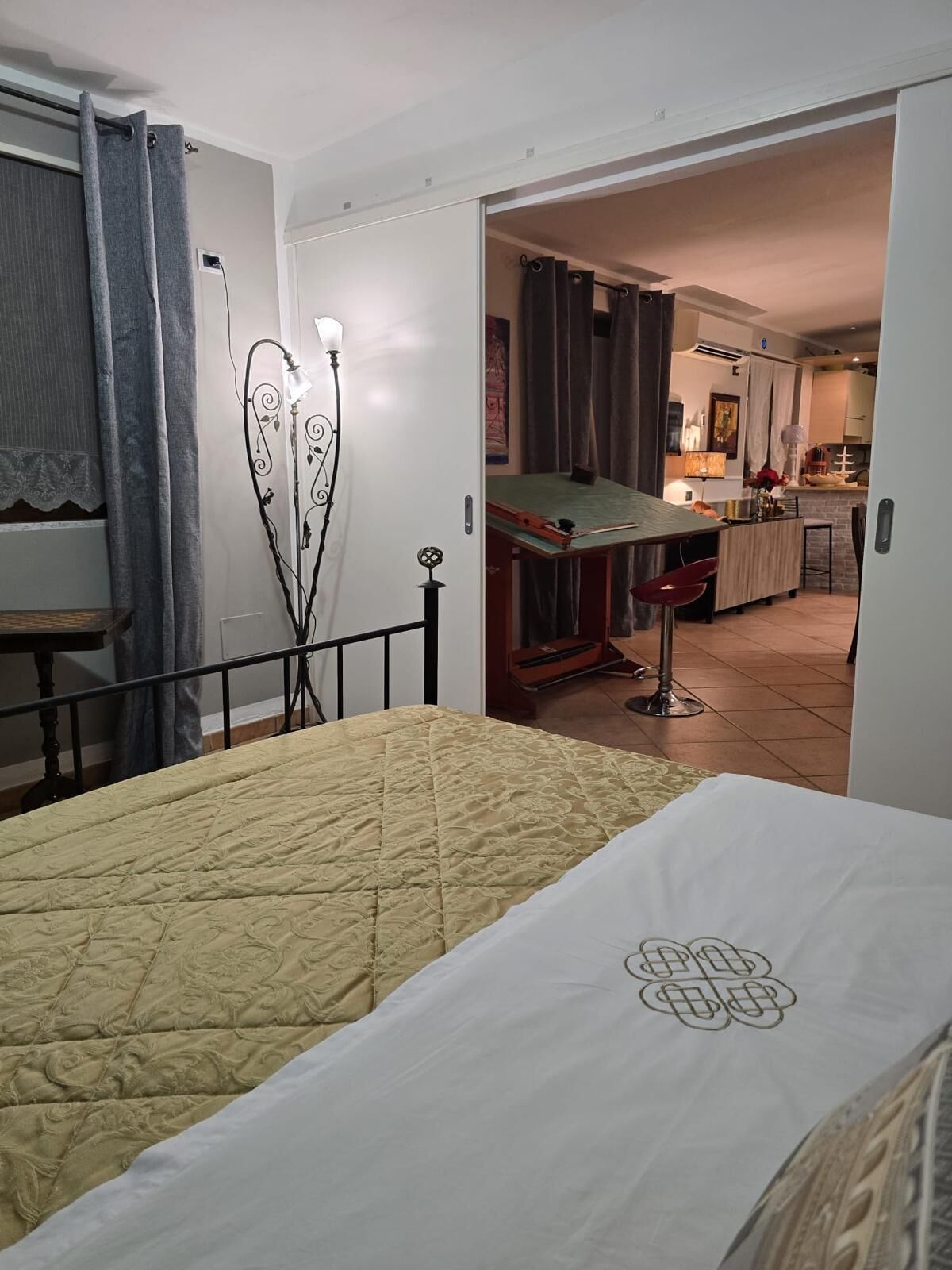 Une chambre à coucher comprenant un lit, une table de chevet et une commode. Une porte donne sur un espace de vie avec une table à manger et des chaises.