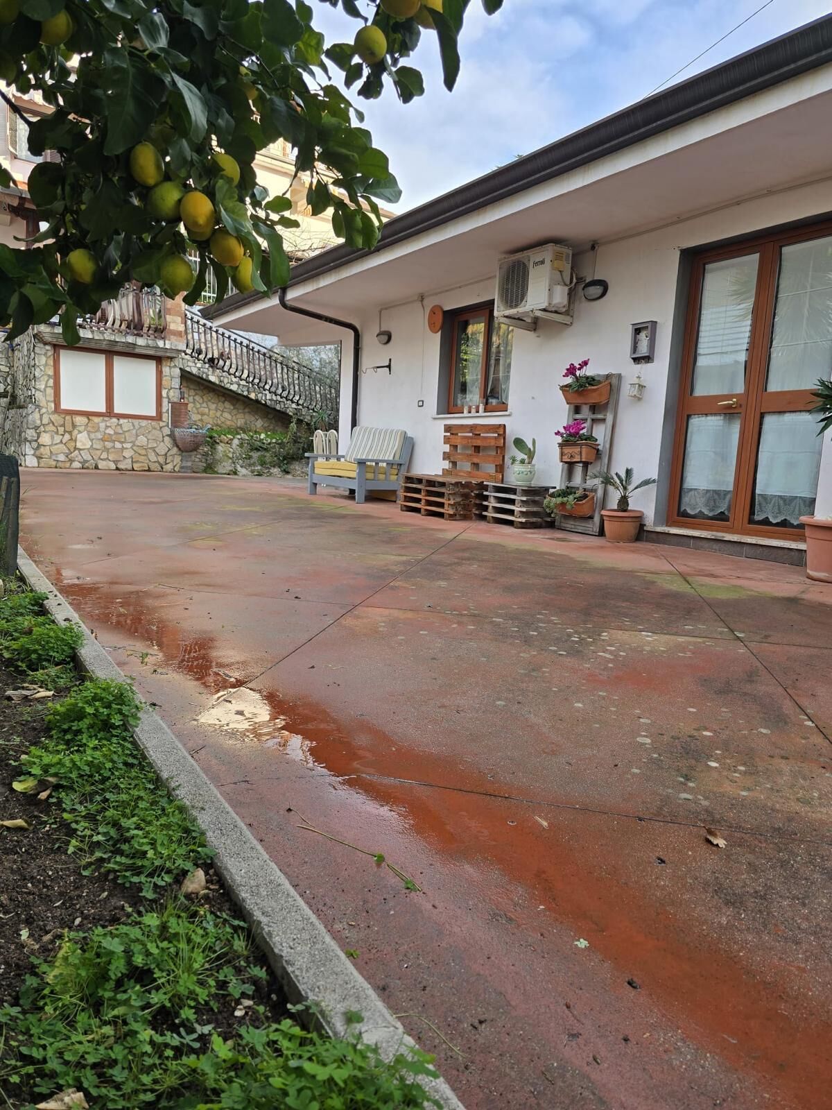 Propiedad residencial con un patio empedrado, un muro de piedra, un banco de madera y plantas en macetas.