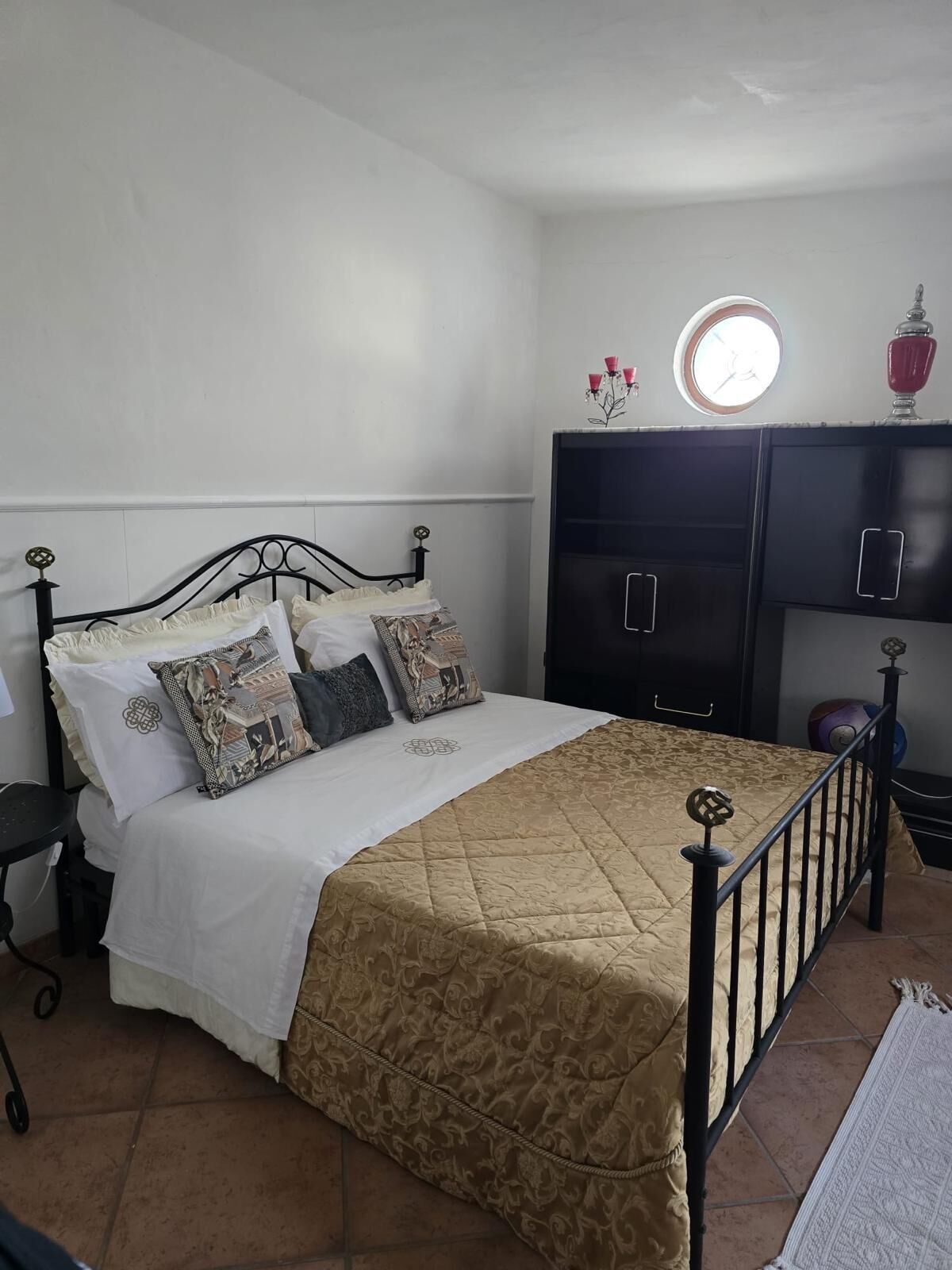 A bedroom with a bed, a nightstand, a wardrobe, and a small round mirror on the wall.