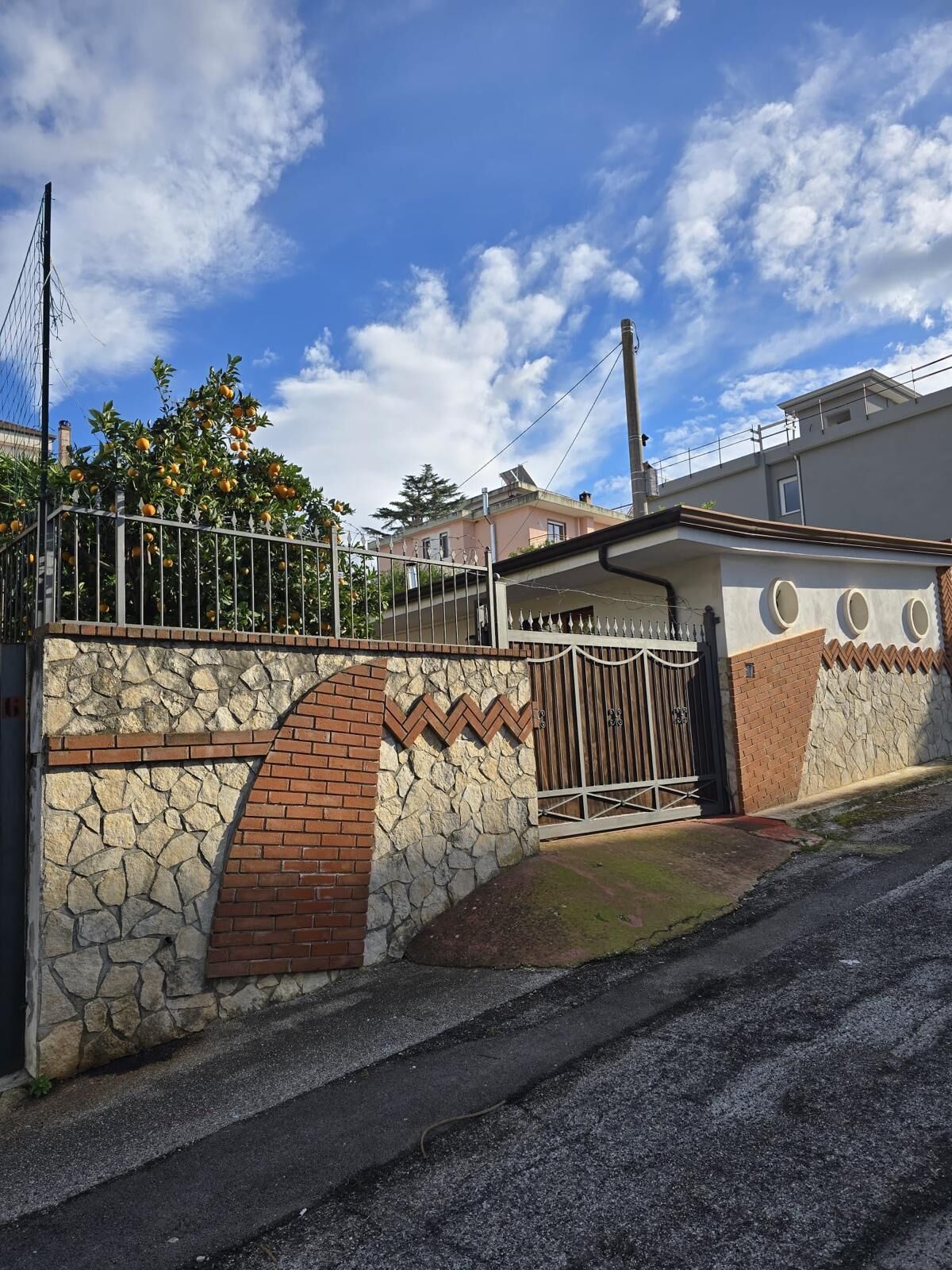 A gated residential area with a stone wall, a metal gate, and a paved driveway.