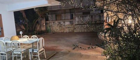 An outdoor patio with a dining table and chairs, surrounded by stone walls and vegetation.