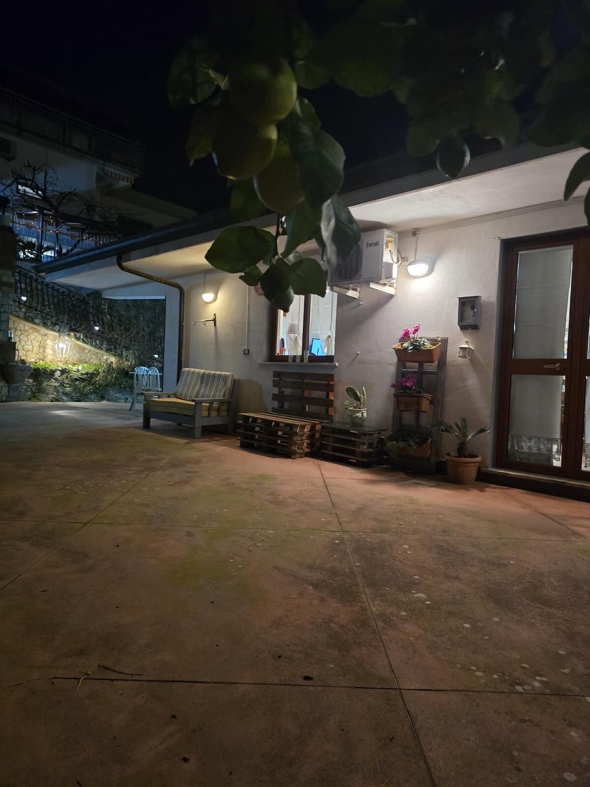 Un espace extérieur abrité, doté d’un banc, de plantes en pot et d’un climatiseur fixé au mur.