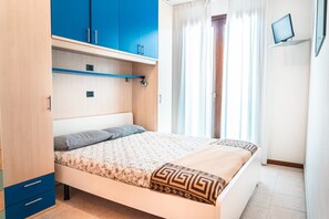 A bedroom with a bed, a wardrobe, a television, and a window with curtains. - Cozy Flat With Pool Access (San Michele al Tagliamento)