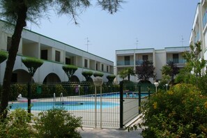 A pool area with a fenced pool, surrounded by greenery and buildings with balconies. - Cozy Flat With Pool Access (San Michele al Tagliamento)