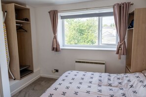 A bedroom with a bed, a window with curtains, a radiator, and a wardrobe. - Comfortable Flat In Devonport Wifi Full Kitchen (Plymouth)