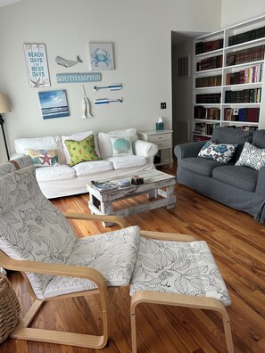 A living room with a white sofa, a grey sofa, and a wooden coffee table. There is a bookshelf filled with books and a wall with decorative items. - Charming 3-bedroom house in peaceful Southampton with AC and amenities (Southampton)